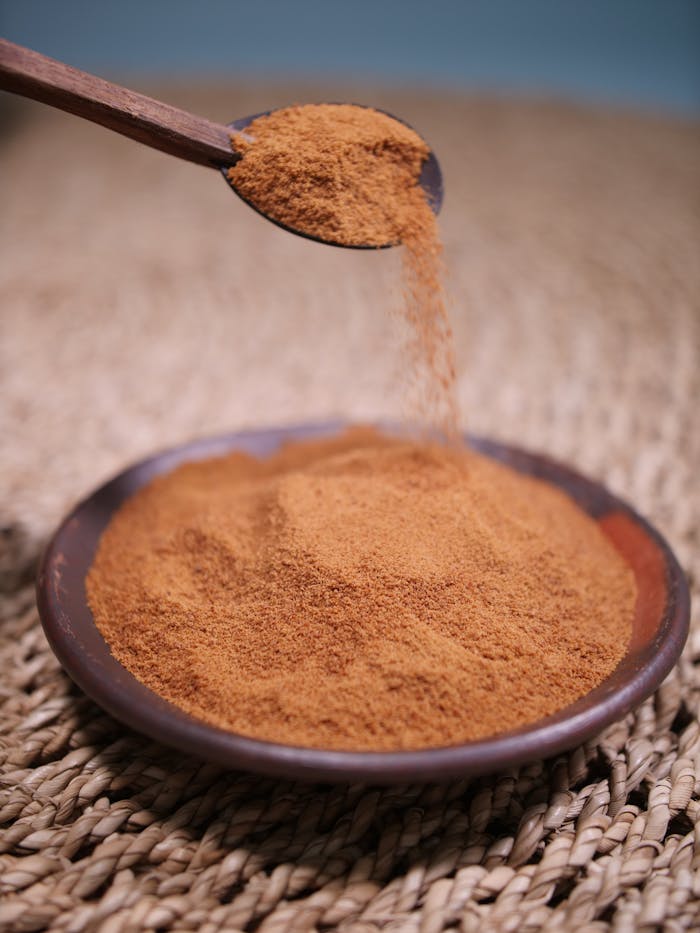 Home A close-up of cinnamon powder being poured from a spoon into a rustic wooden bowl, ideal for recipes.